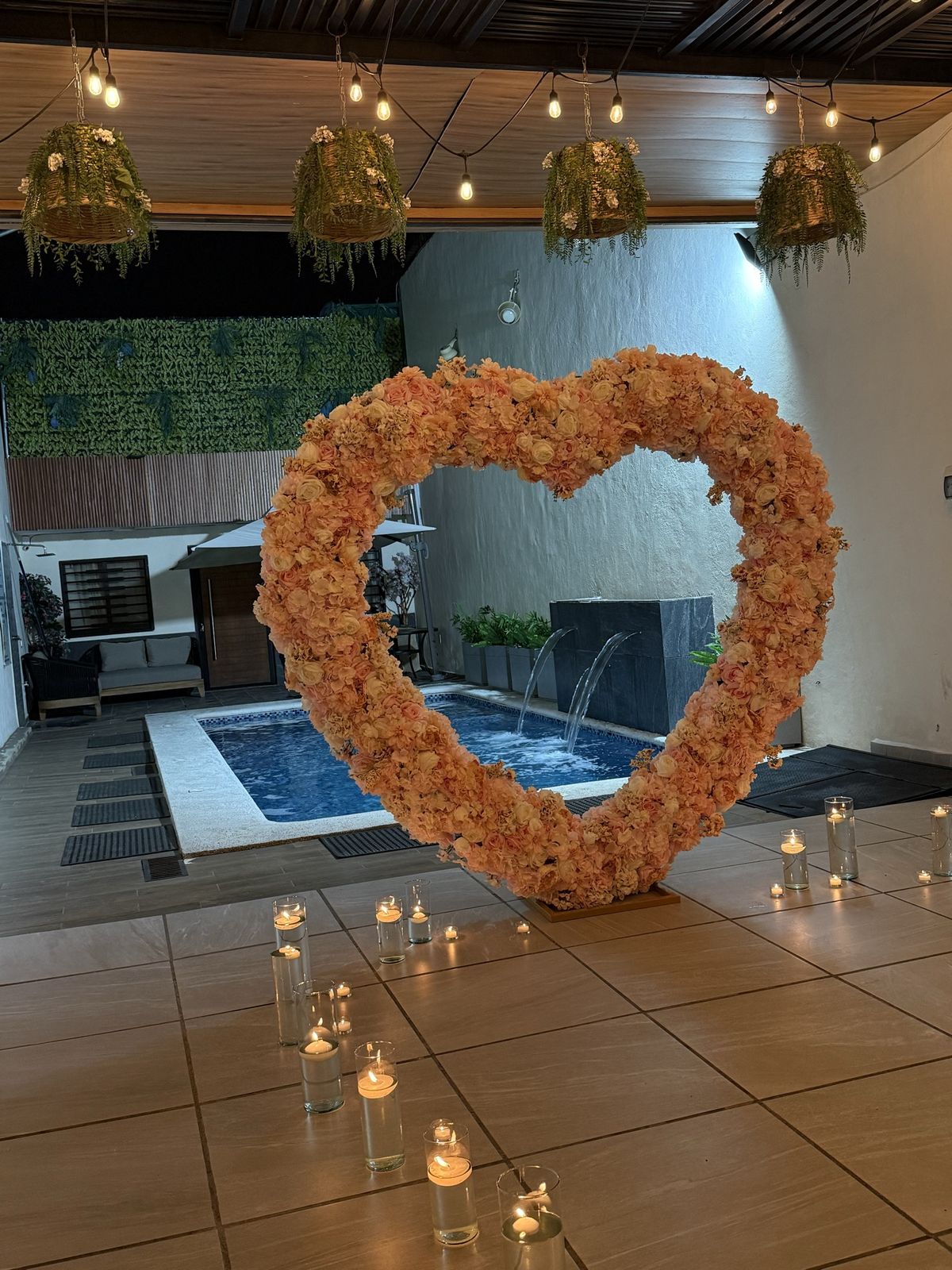 Corazón de flores de durazno frente a la alberca iluminada, con camino de velas encendidas, en Terraza Plutarco