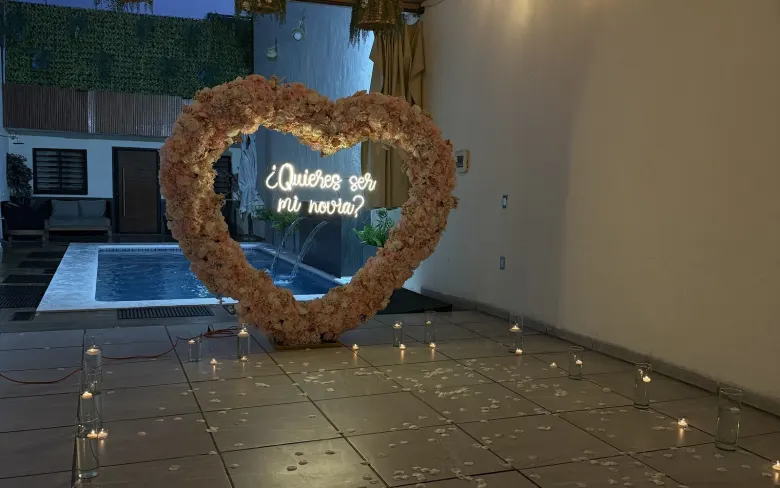 El corazón de flores con el neón encendido frente a la alberca iluminada, con velas en el piso de la terraza
